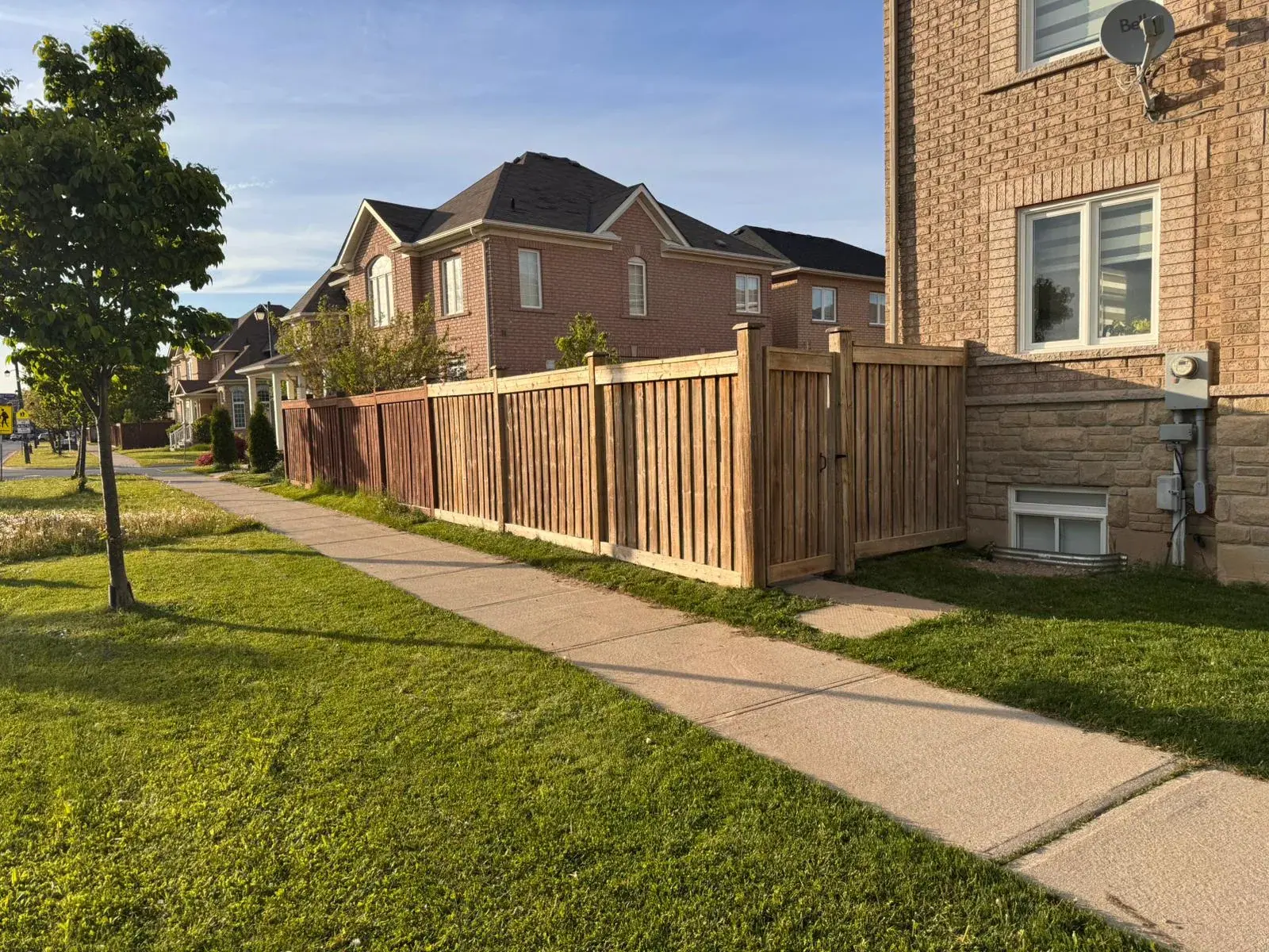 Wooden fence and gate beside a sidewalk and brick homes
