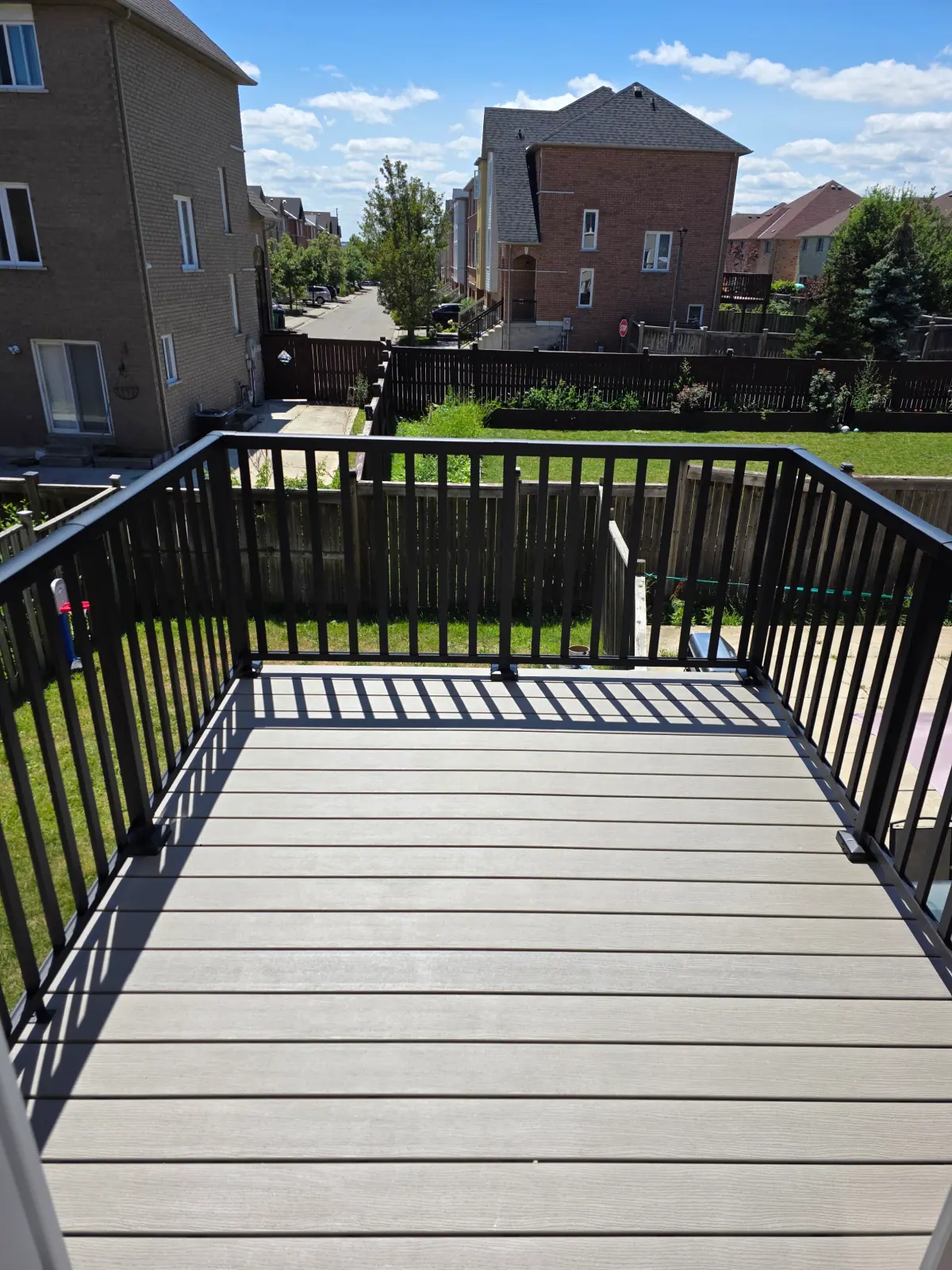 Deck boards and black metal railings overlooking a fenced backyard