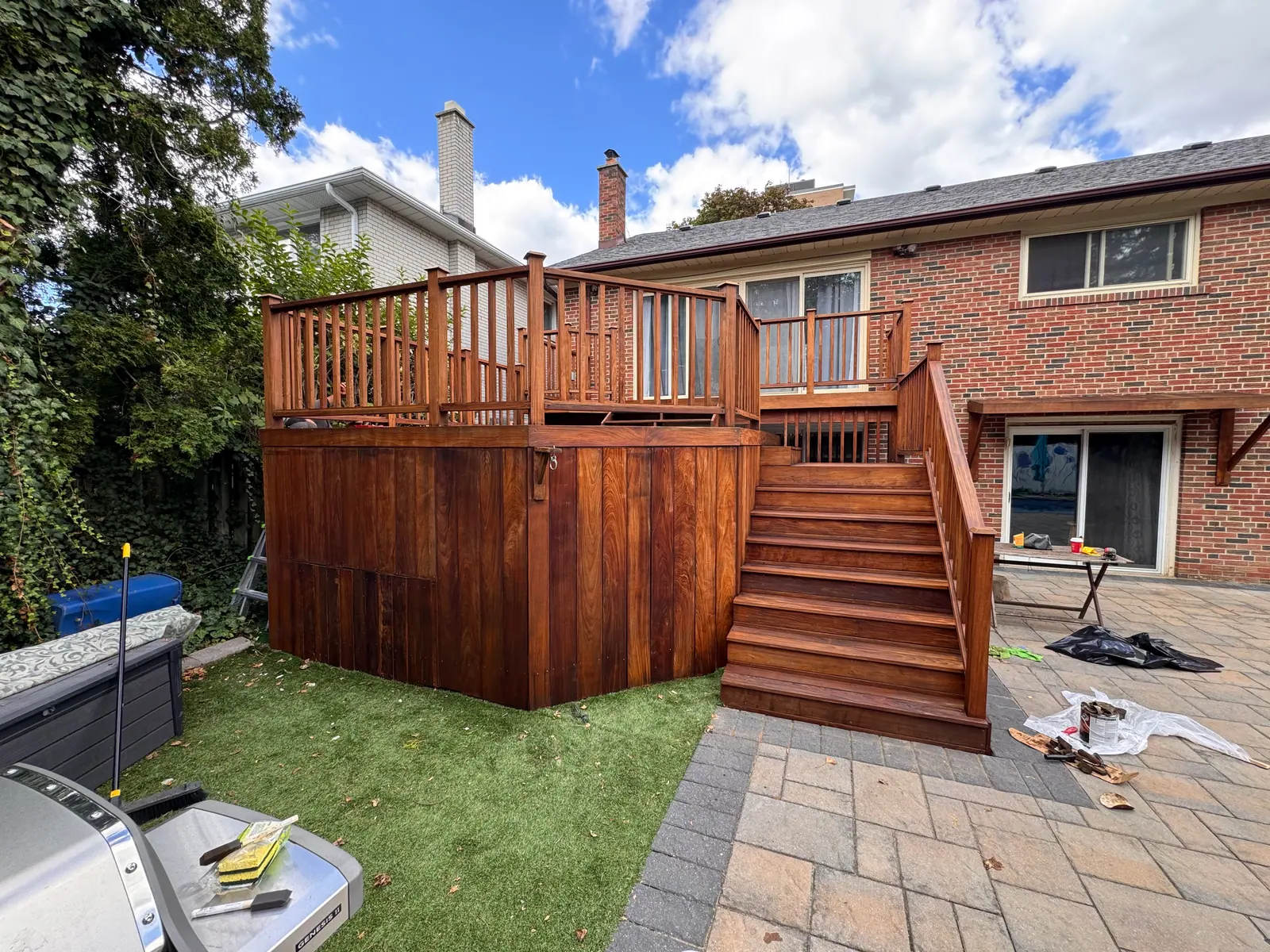 Stained raised wood deck with railings and broad stairs leading to the patio