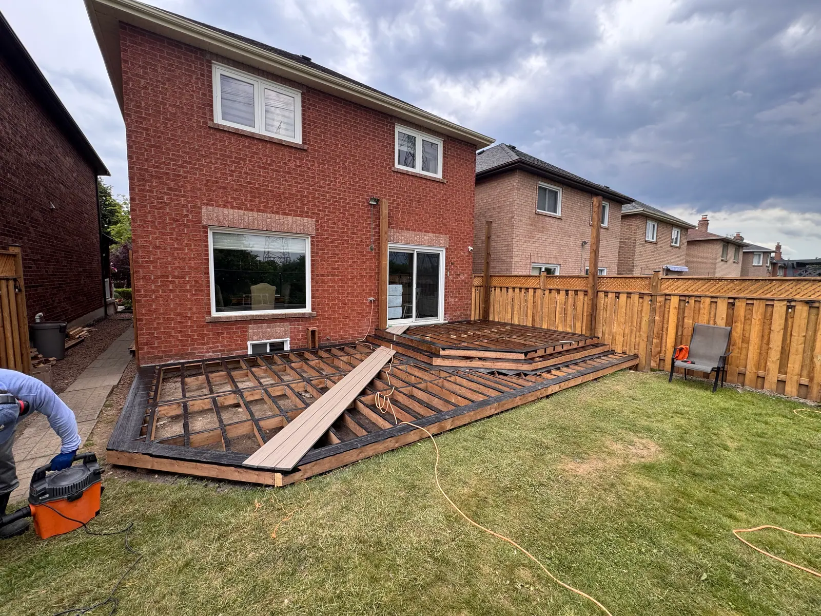 Backyard deck framing and boards being installed beside a brick house